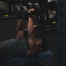An adult man performing a dumbbell exercise on a bench inside a gym, focusing on strength and fitness.