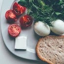 Flat lay of fresh tomatoes, boiled eggs, herbs, and bread representing a healthy breakfast.