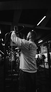 A man exercising with gym equipment indoors, captured in dramatic black and white tones.